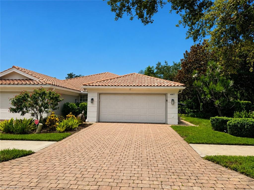Elegant single-story residence showcasing a wide two-car garage with paneled doors, barrel tile roof, and neutral stucco exterior