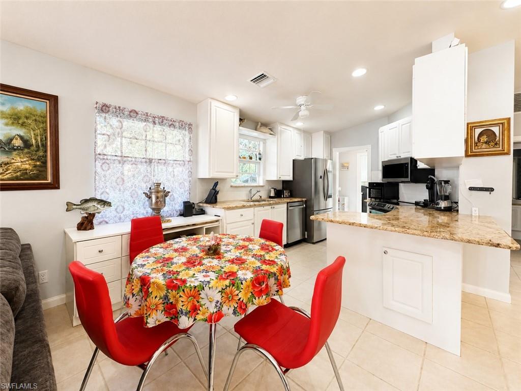 Kitchen featuring white cabinetry, light-toned flooring, granite-finish countertops, stainless steel appliances, and a breakfast bar with built-in storage