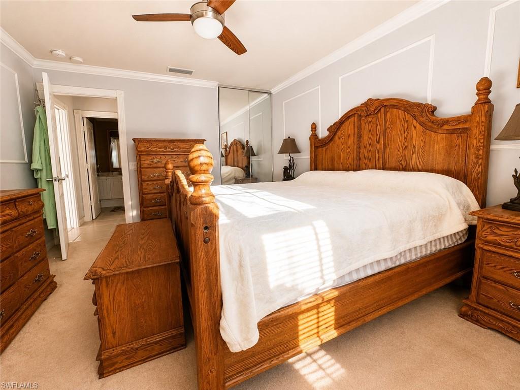 Spacious primary bedroom featuring solid wood furnishings, white bedding, carpet flooring, ceiling fan with integrated lighting, and abundant natural light from multiple windows