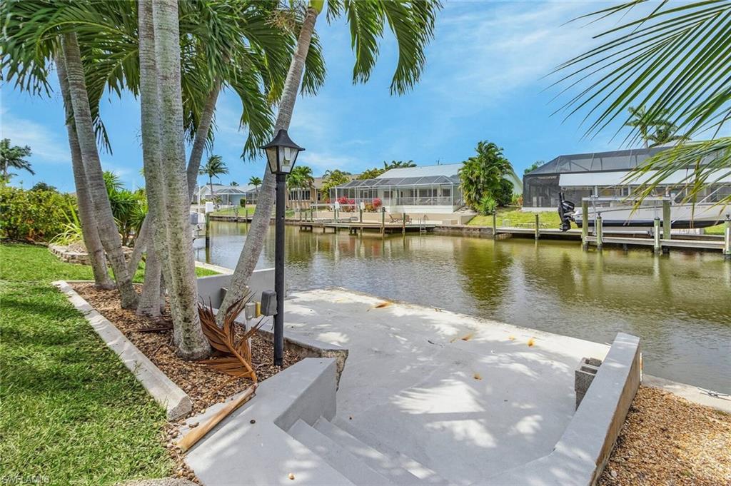 Waterfront property with concrete steps, palm trees, and a built-in lamp post