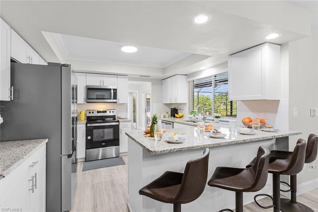 Modern kitchen with white cabinetry, stainless steel appliances, light-toned wood-finish flooring, recessed lighting, and an island with a light-toned countertop