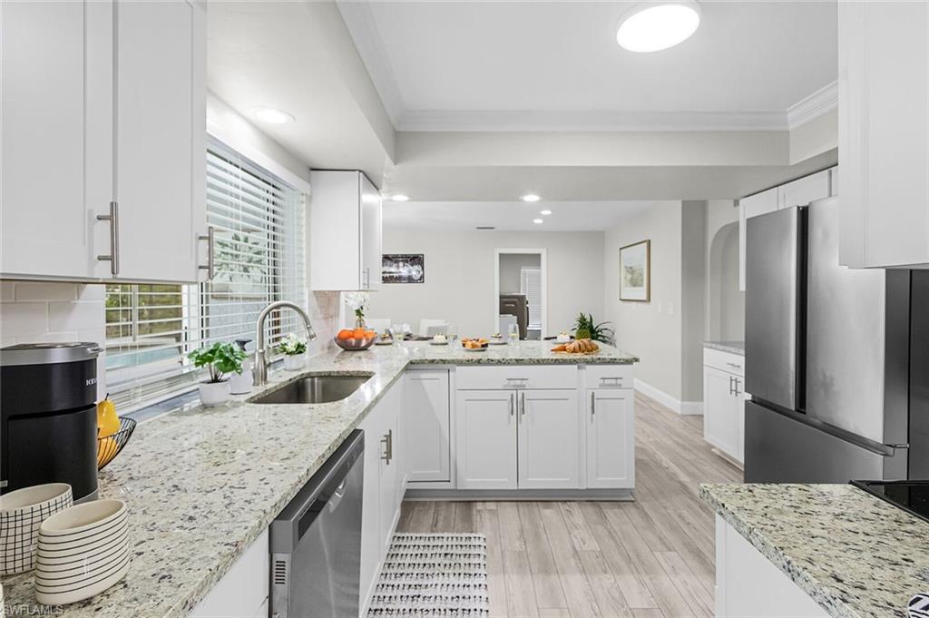 Bright kitchen featuring white shaker cabinetry, stainless steel appliances, a multi-level island with a light-toned countertop, and wood-finish flooring