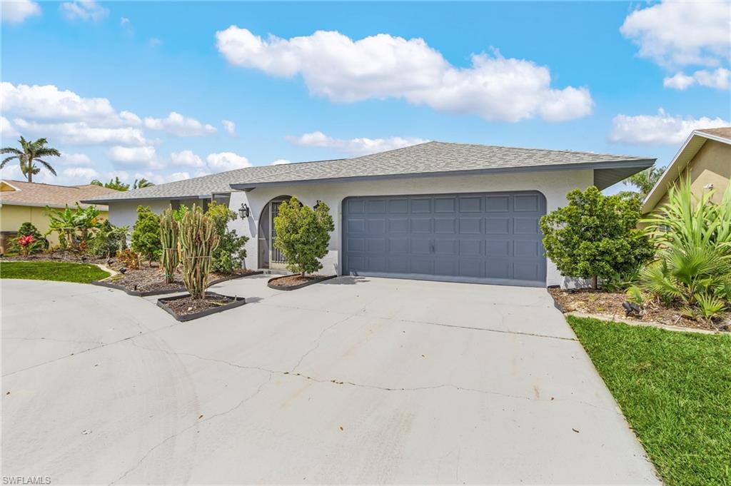 Exterior featuring a gray garage door, arched entryway, and mature landscaping