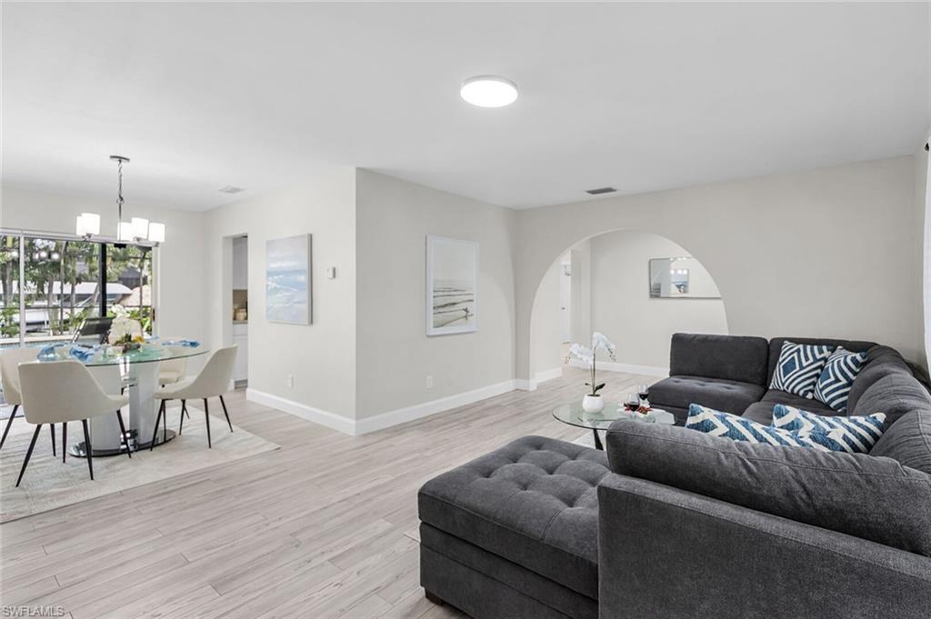 Open-concept living space featuring wood-finish flooring, a modern chandelier, and large windows