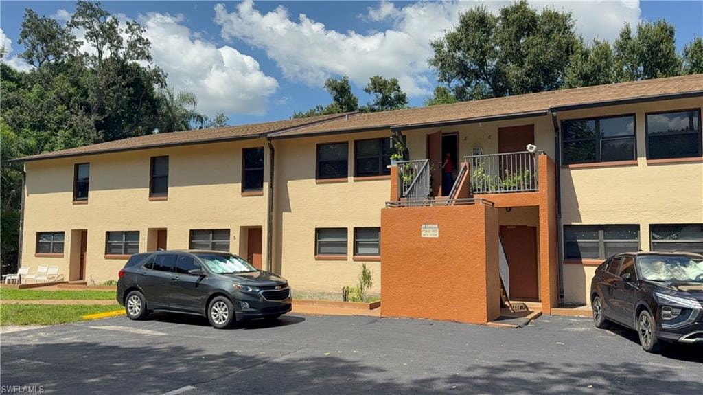 Two-story multi-unit property with a neutral stucco exterior, covered stairwell access, and an upper-level balcony with metal railing