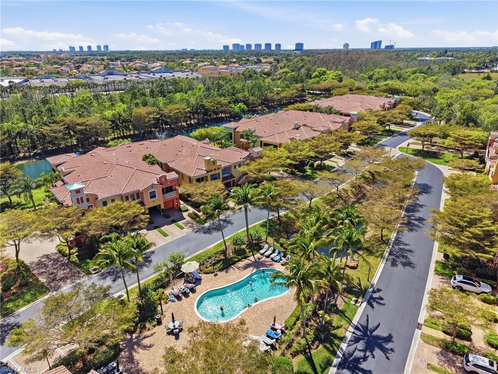 Community featuring a curvilinear swimming pool, mature palm trees, paved roadways, and multi-story residences with terracotta tile roofs