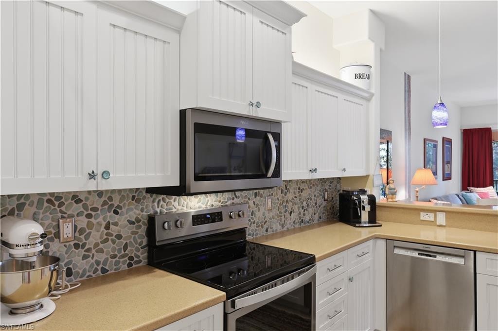 White cabinetry with beadboard paneling, stone pebble mosaic backsplash, stainless steel appliances, and light-toned countertops