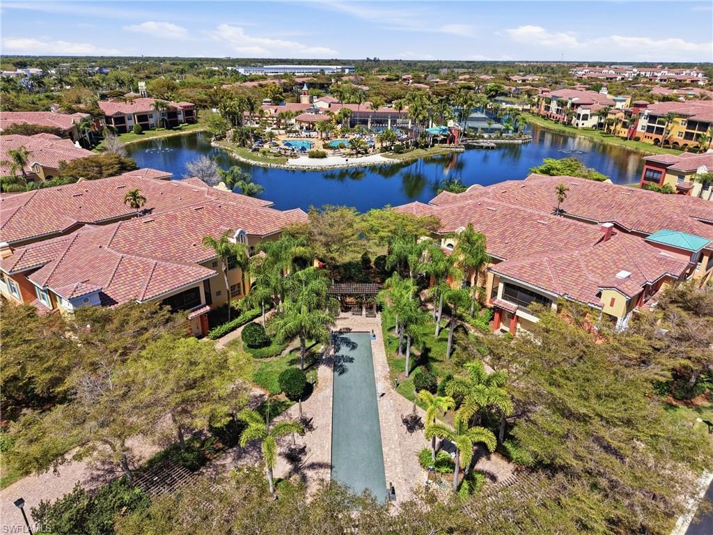 Community featuring multiple buildings with tile roofs, a central water body, outdoor swimming pools, and extensive landscaping with mature trees