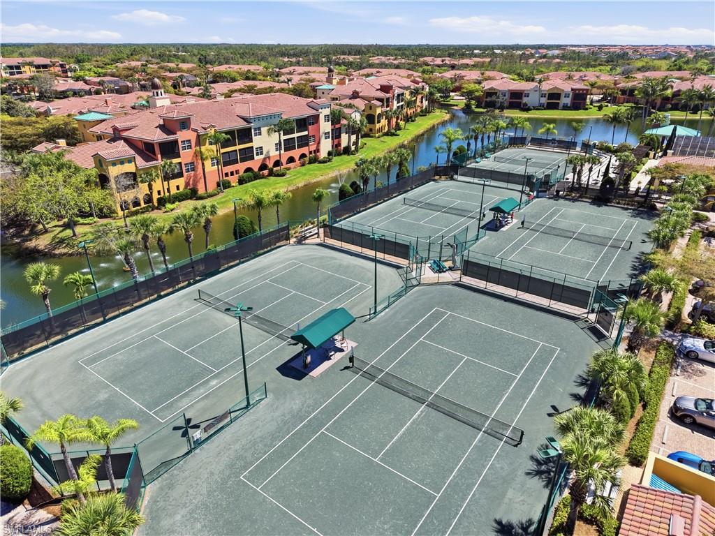 Multiple tennis courts with perimeter fencing, shaded seating areas, and adjacent water features