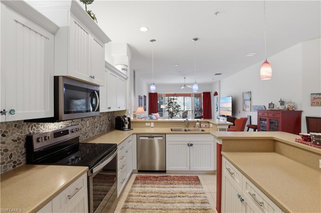White cabinetry with beadboard accents, stone tile backsplash, stainless steel appliances, neutral countertops, and recessed lighting