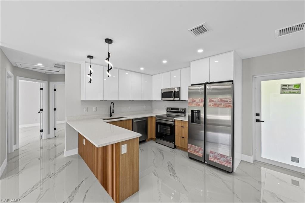 Kitchen featuring white high-gloss upper cabinetry, wood-finish lower cabinetry, a white countertop peninsula, and stainless steel appliances