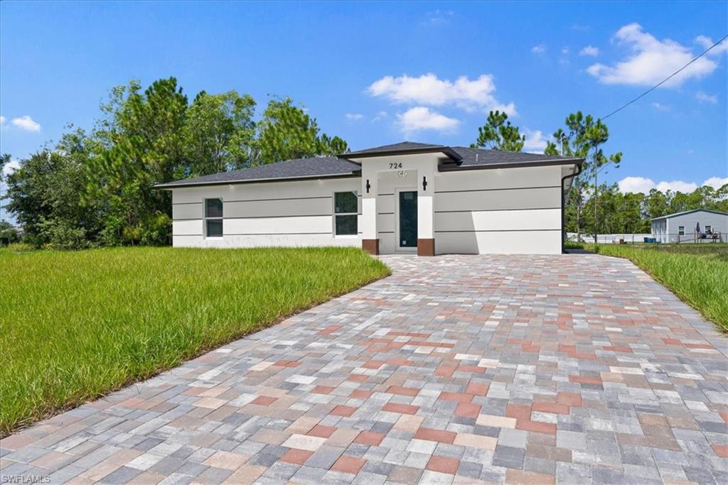 Modern residence featuring a striking geometric facade with clean lines and neutral exterior finishes, complemented by an expansive permeable paver driveway in a mixed-tone brick pattern
