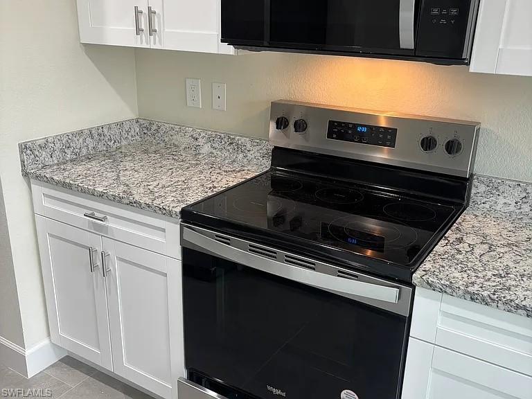 Modern kitchen featuring stainless steel electric range with smooth cooktop, granite-style speckled countertops, white cabinetry with brushed metal hardware, and under-cabinet warm lighting