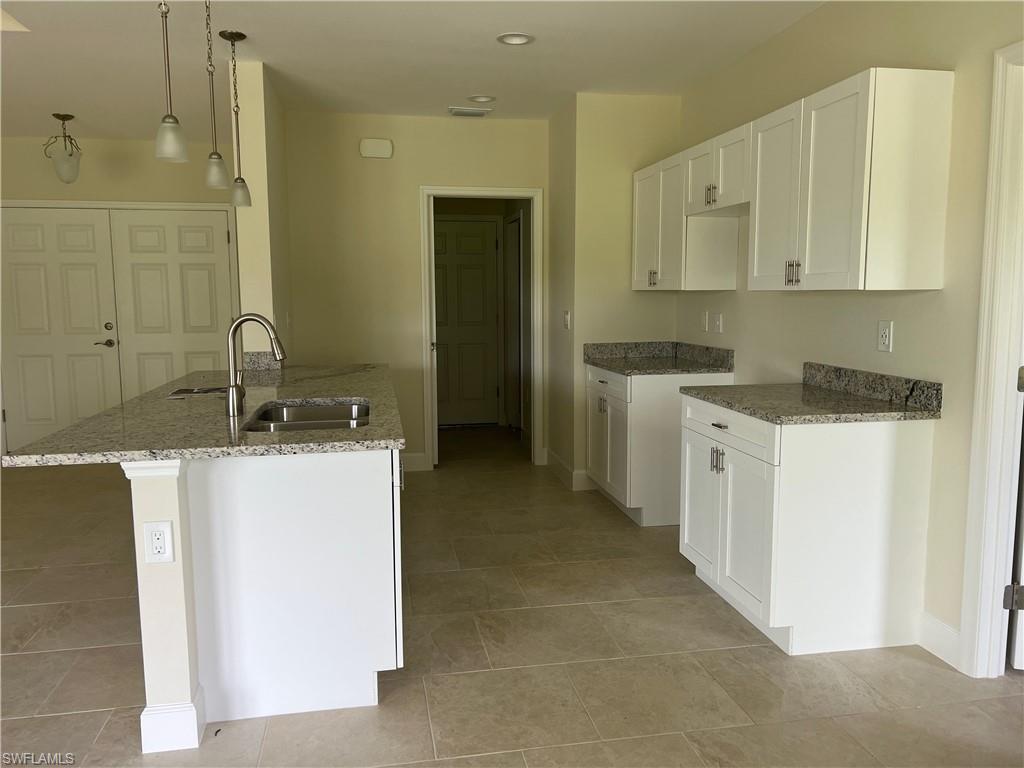 Kitchen featuring white shaker cabinetry, speckled countertops, a double basin sink with a high-arc faucet, and tiled flooring