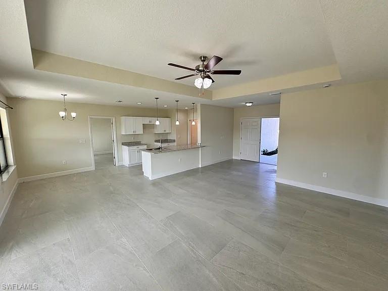 Open-concept living area with large format tile flooring, a kitchen featuring white cabinetry, a central island with pendant lighting, and a ceiling fan