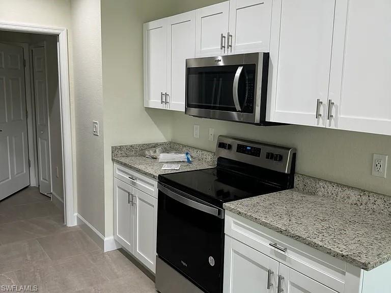 Updated kitchen featuring white cabinetry with brushed nickel hardware, granite countertops, stainless steel appliances including a black electric range and built-in microwave, and neutral tile flooring