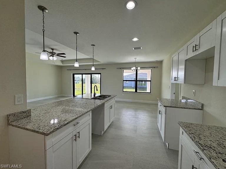 Spacious kitchen featuring white cabinetry, granite-style countertops, stainless steel appliances, and pendant lighting suspended from a coffered ceiling