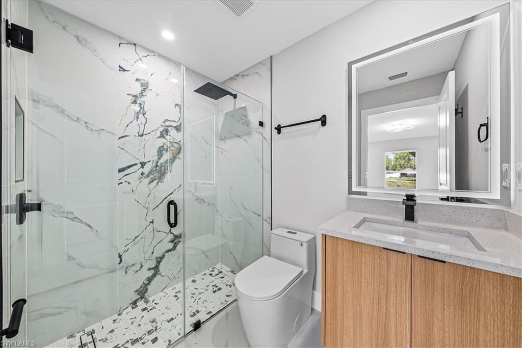 Glass-enclosed shower with large format marble-look tile and mosaic flooring