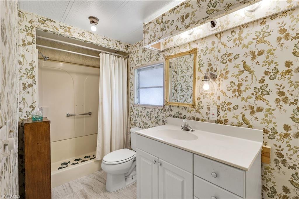 Bathroom featuring a full vanity with an integrated sink, a built-in tub with a shower, a framed wall mirror, and a window