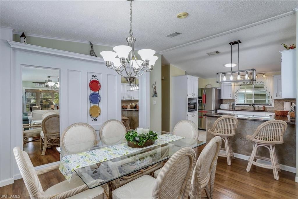 Dining area with wood-look flooring, a chandelier, and wall moulding open to kitchen.