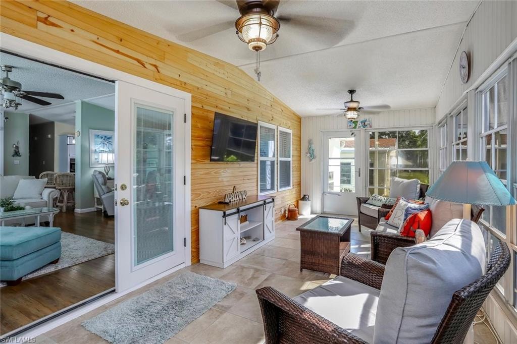 Screened porch featuring light-toned tile flooring, light wood paneling, multiple windows, a ceiling fan, and French doors