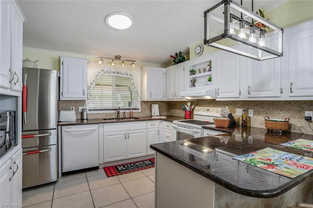 White cabinetry, stainless steel appliances, granite countertops, tile flooring, sun tunnel and a modern light fixture.