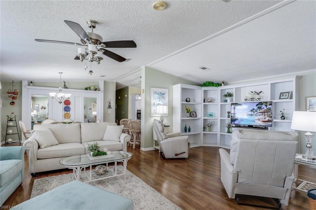 Spacious living area featuring wood-look flooring, built-in shelving, a ceiling fan with integrated lighting, and flow from kitchen to dining room to living room to Florida room.
