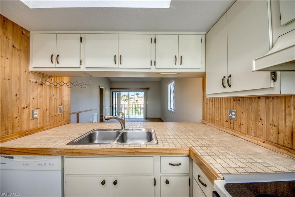 Kitchen with wood walls, sink, dishwasher, and white cabinets