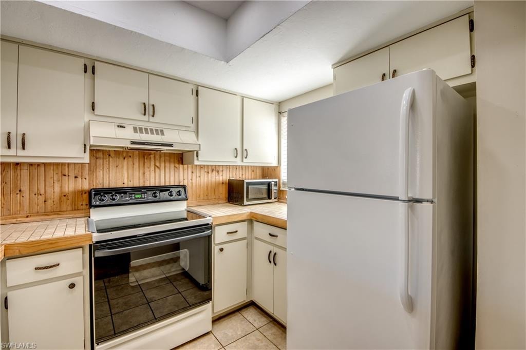 Kitchen featuring white cabinetry, light tile patterned floors, and white appliances