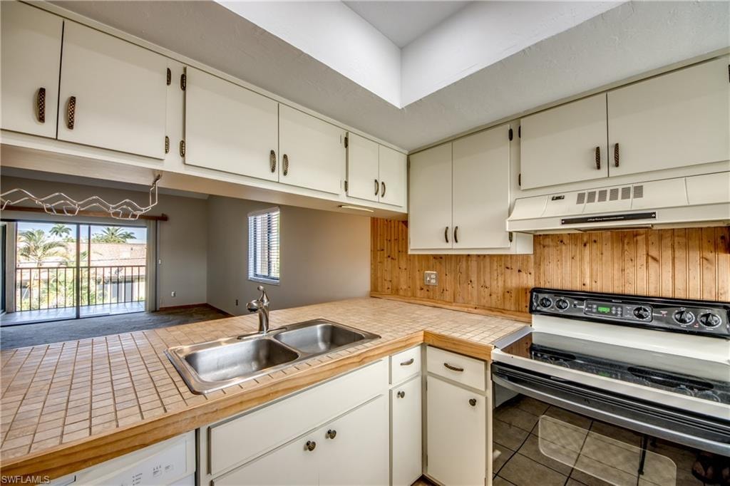 Kitchen featuring white cabinetry, kitchen peninsula, electric stove, tile patterned floors, and sink