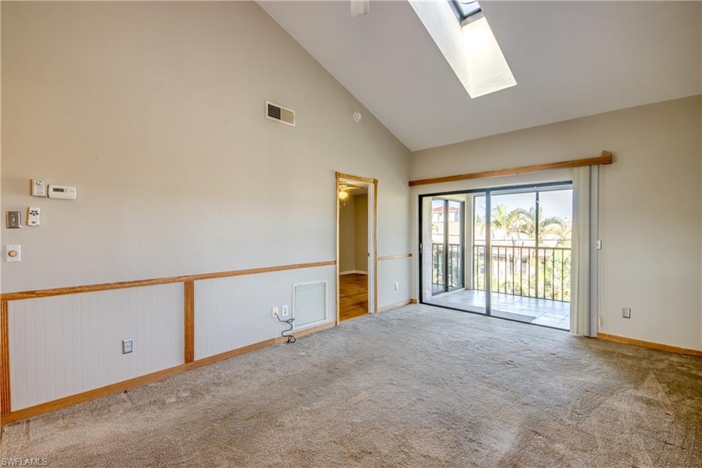 Unfurnished room featuring high vaulted ceiling, carpet, and a skylight