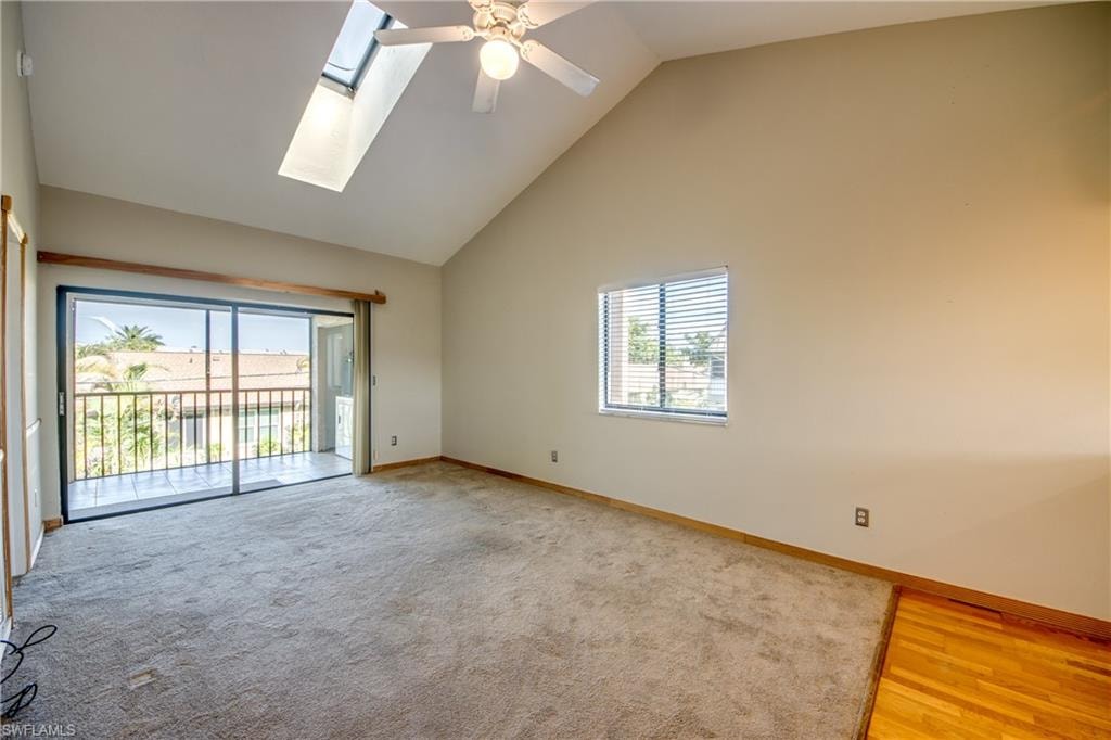 Empty room with a skylight, light hardwood / wood-style floors, high vaulted ceiling, and ceiling fan