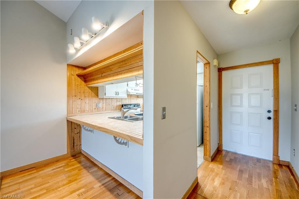 Kitchen with sink, backsplash, white cabinets, and light wood-type flooring