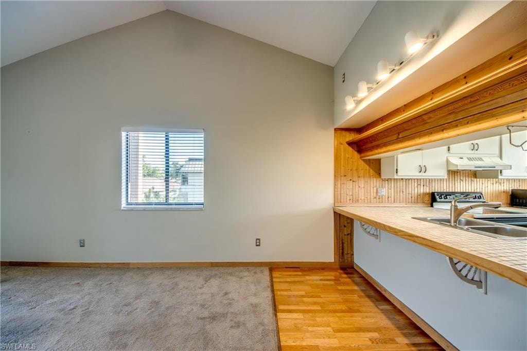 Kitchen featuring white cabinets, lofted ceiling, stove, and light wood-type flooring