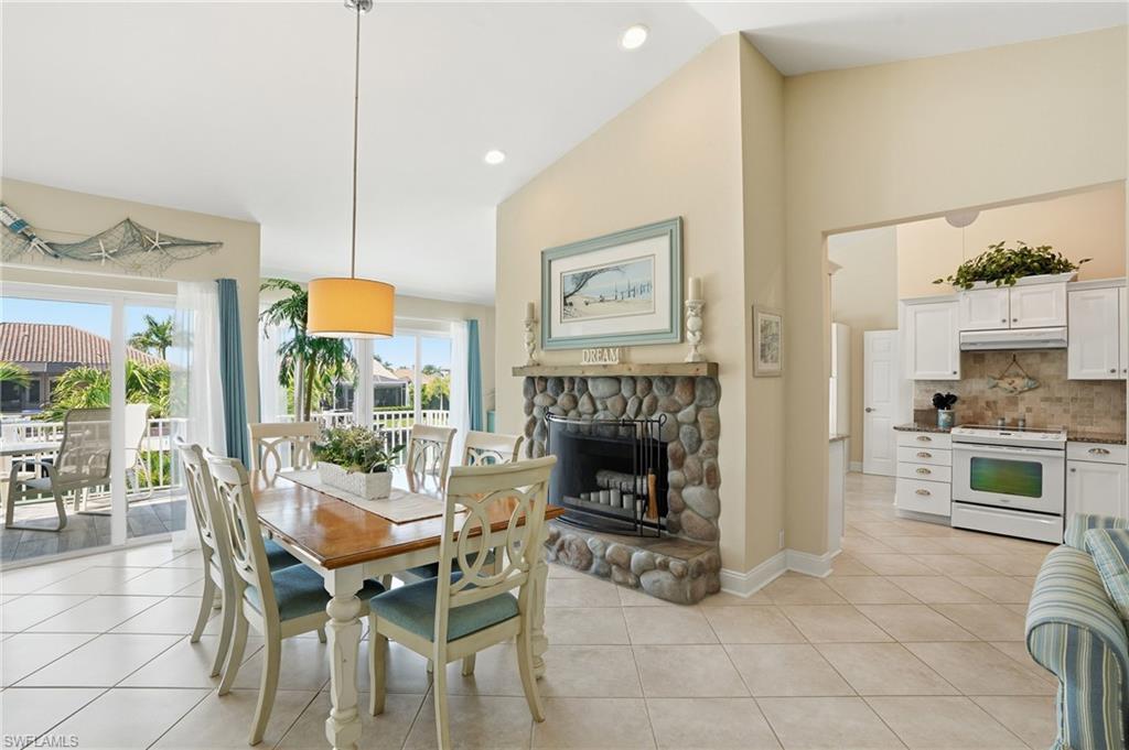 Vaulted ceilings, a stone-faced fireplace, and tile flooring define this dining area, with sliding glass doors leading to an outdoor balcony