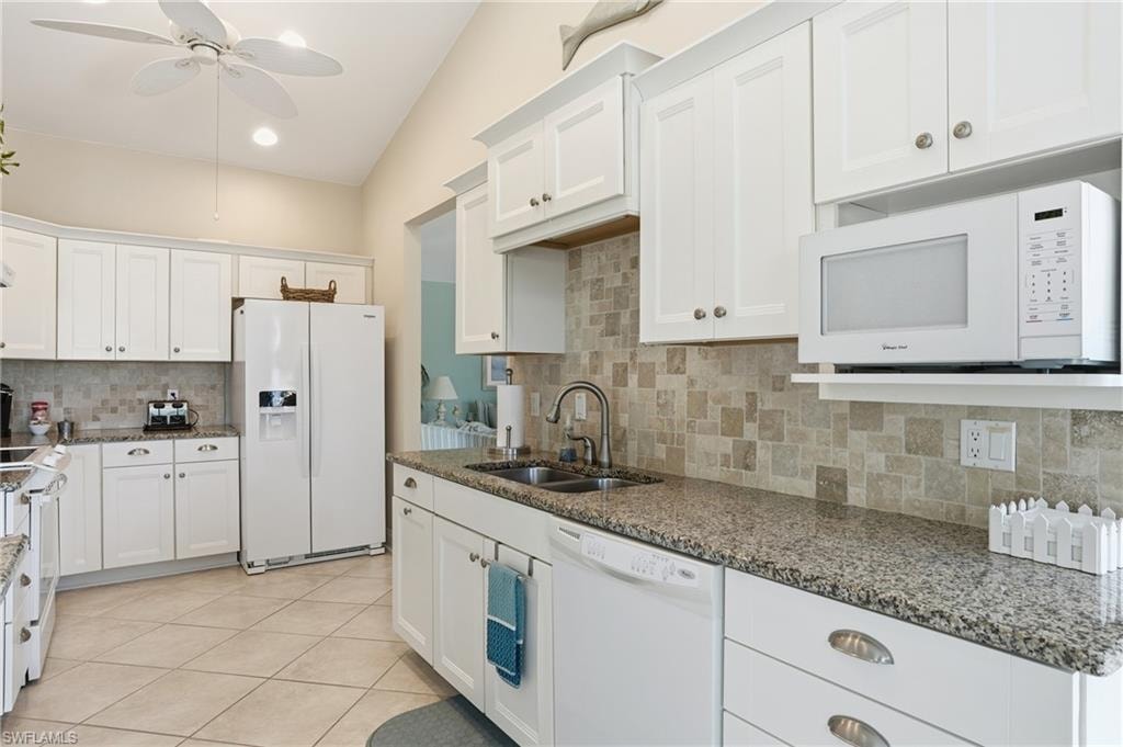 Kitchen featuring white cabinetry, speckled countertops, tile backsplash, tile flooring, and vaulted ceiling