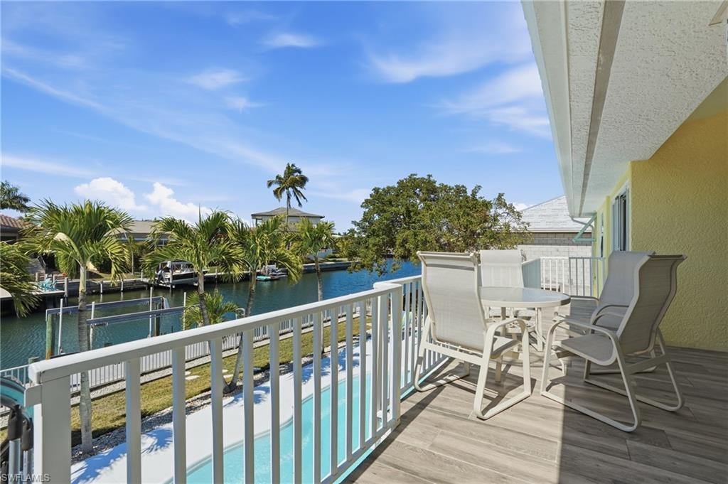 Balcony with wood-finish flooring and white railing, overlooking a canal and an adjacent swimming pool