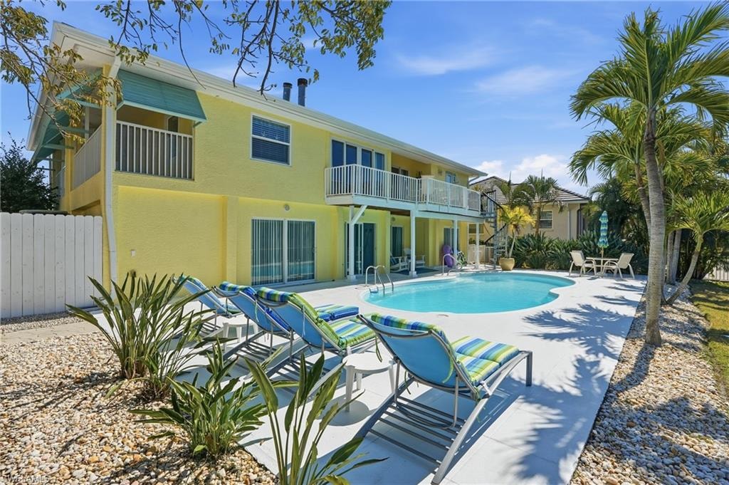 Expansive outdoor living area featuring a kidney-shaped pool, concrete patio, mature palm trees, and a white privacy fence