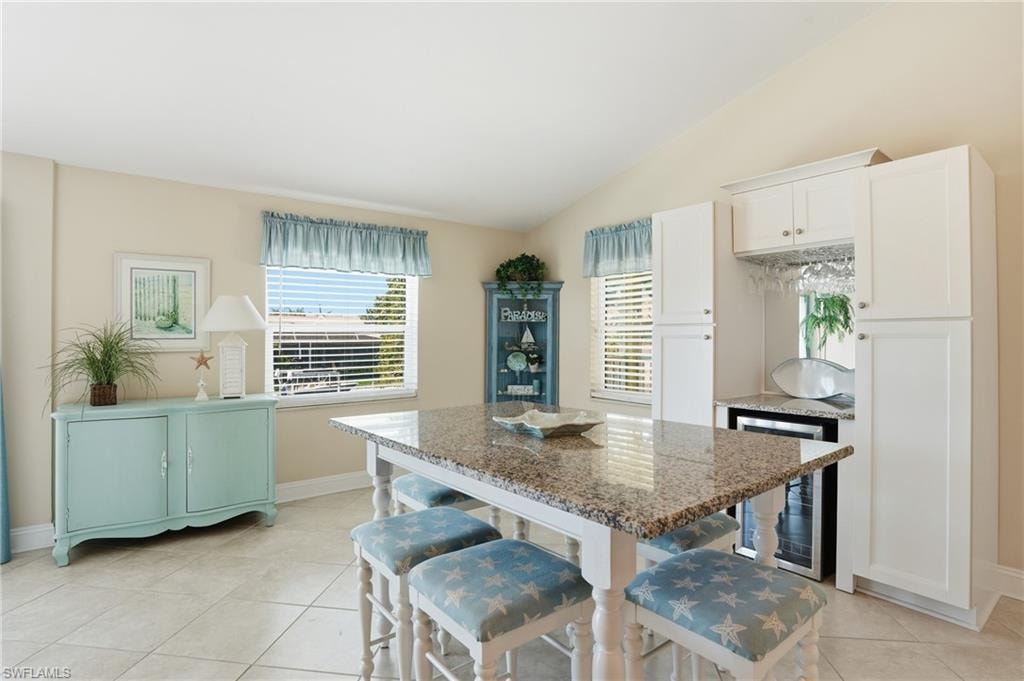 Open-concept space featuring vaulted ceilings, tile flooring, a built-in wet bar with a beverage cooler, and a kitchen island with a granite countertop