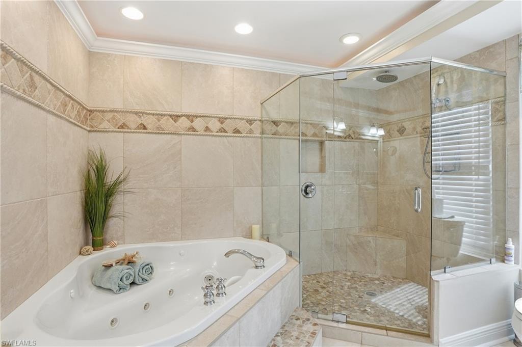 Corner jetted tub with tiled surround, glass-enclosed shower with a built-in bench, tiled walls with decorative mosaic accents, and recessed lighting