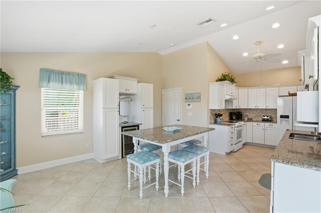 Vaulted ceiling with recessed lighting and ceiling fan, white paneled cabinetry, granite countertops, tile flooring, and a built-in beverage cooler
