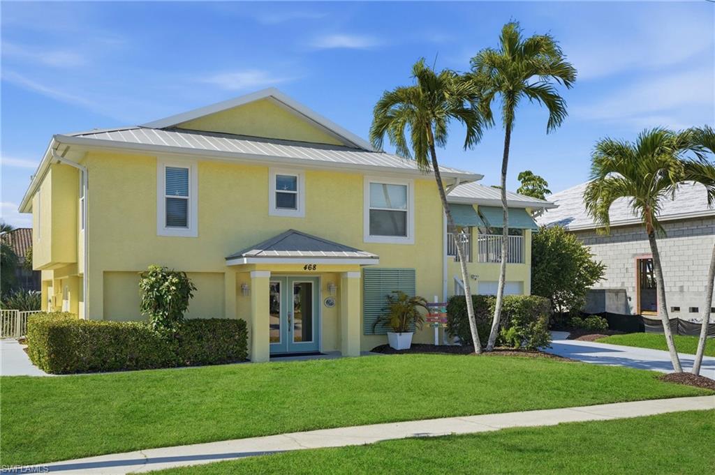Two-story residence featuring stucco exterior, light blue double-entry doors, a balcony with a white railing, and a metal roof