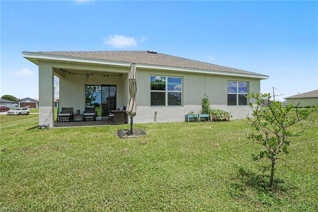 Expansive rear lawn, covered patio, sliding glass door access, and multiple windows with room for a pool.