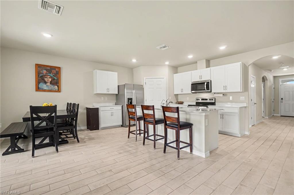 Open-concept kitchen featuring white cabinetry, stainless steel appliances, and a central island with a breakfast bar