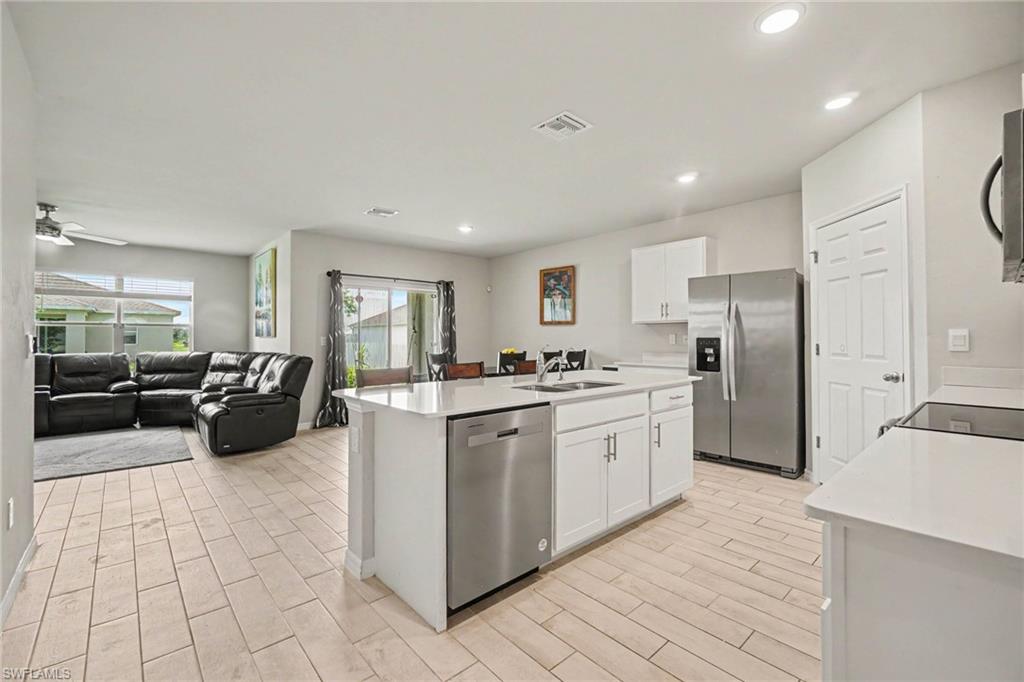 Open-concept layout featuring wood-finish flooring, white cabinetry, and stainless steel appliances