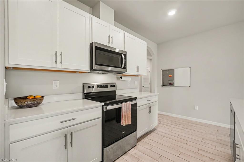 White shaker-style cabinetry, stainless steel microwave, stainless steel range, light-toned countertops, and wood-finish flooring