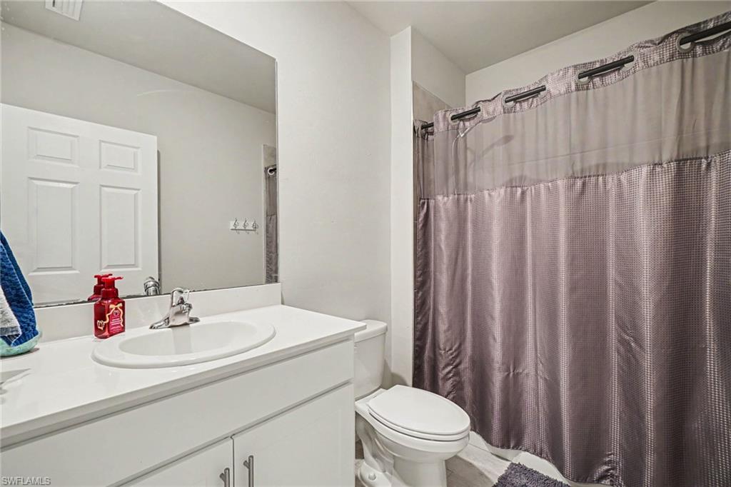 White vanity with integrated sink, chrome faucet, wall-mounted mirror, and a toilet with shower enclosure