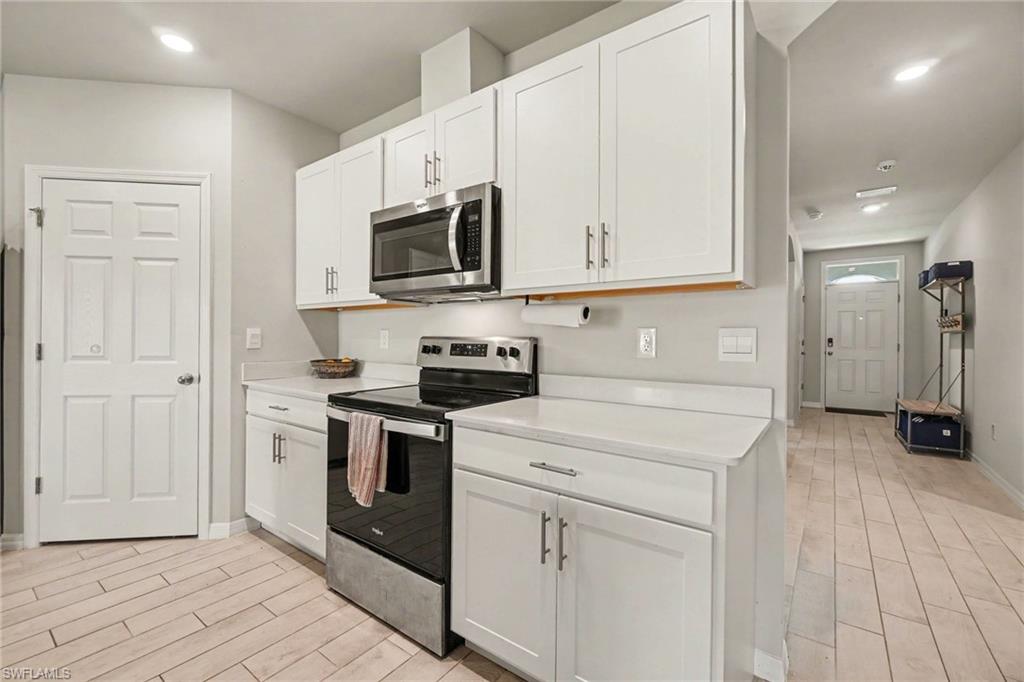 Kitchen with white cabinetry, stainless steel microwave, black electric range, and light-toned tile flooring