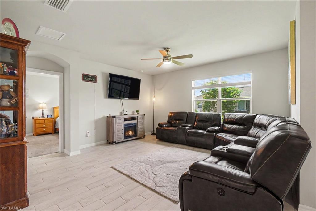 Recessed overhead lighting, ceiling fan, large window with blinds, light-toned tile flooring, and an arched doorway