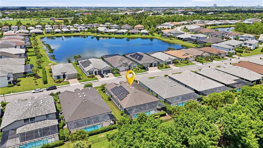 Aerial perspective of a residential community featuring a prominent lake, homes with screened-in pools, and solar panels
